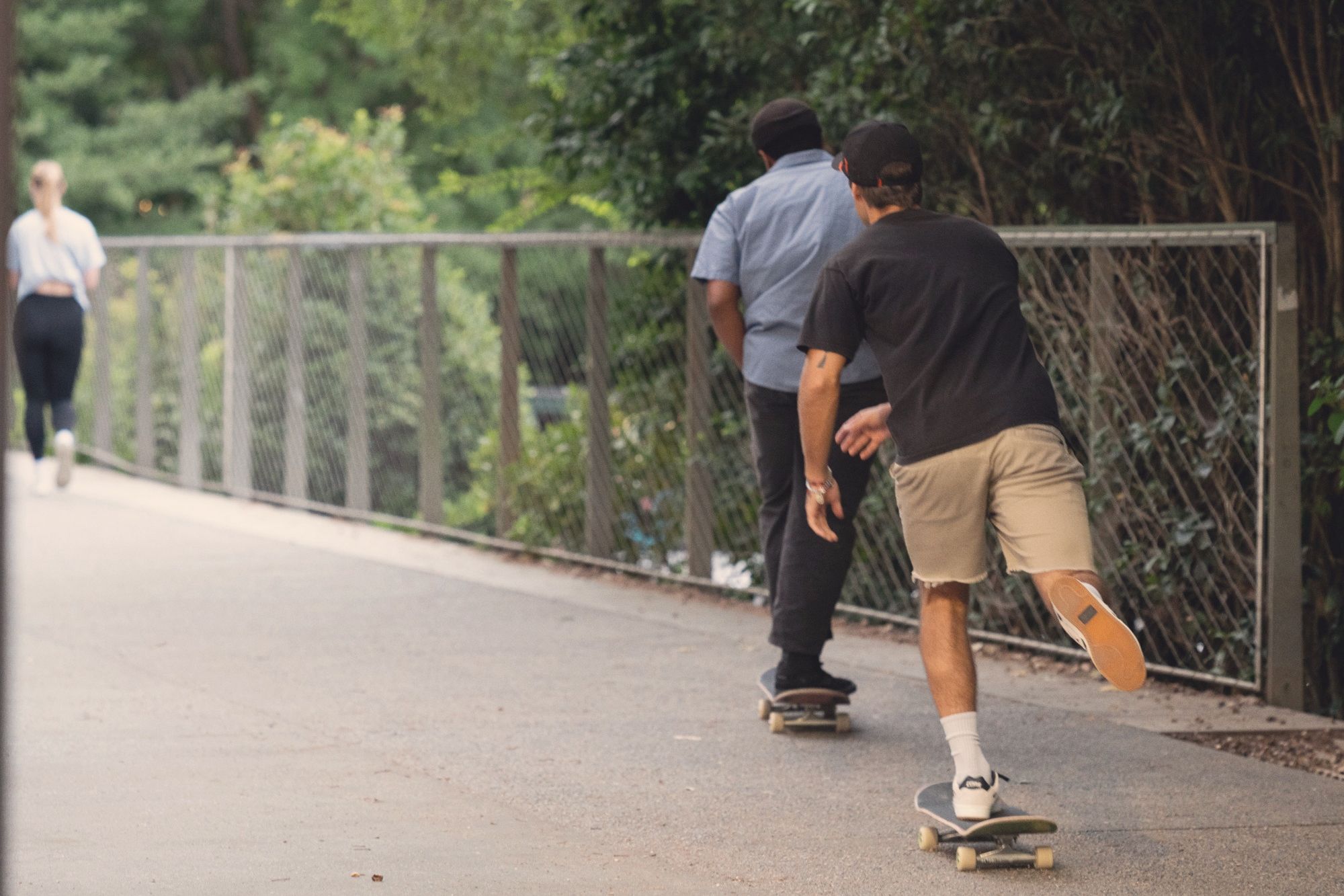 Two skateboarders pushing down a tree-lined stretch of the Beltline trail, a runner up ahead
